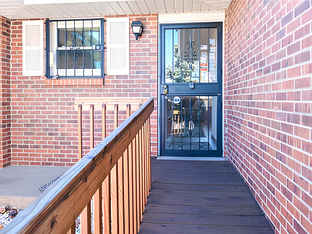 A wooden ramp leads to a glass door set in a brick wall.