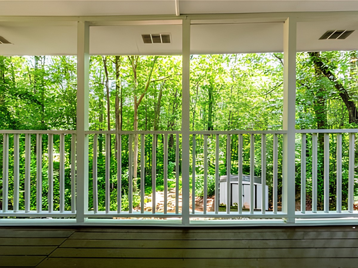 A balcony with white railings overlooks a lush, green forest.