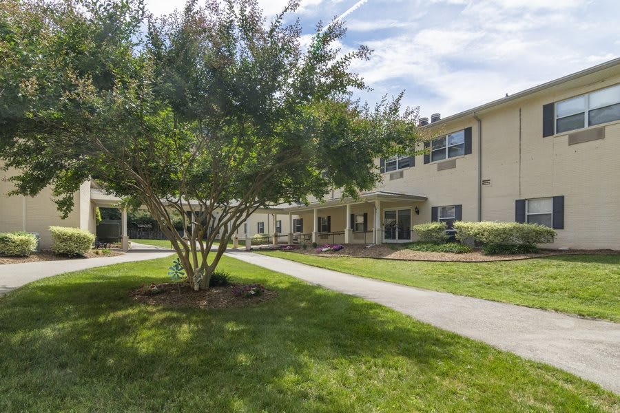 A sunny day view of a residential building with a landscaped lawn and pathway.