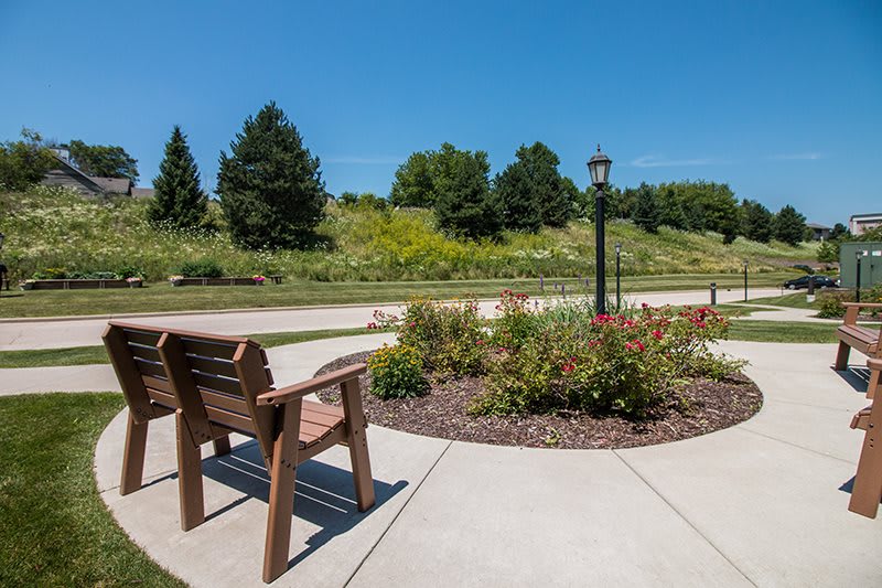 A peaceful garden path with a bench, flowers, and a lamp post under a clear blue sky.