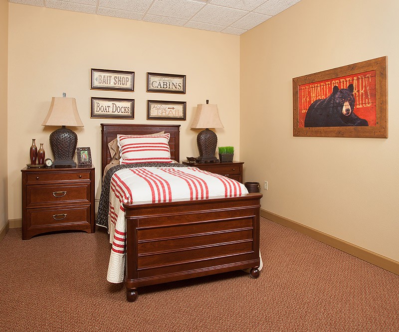 A cozy bedroom featuring a single bed with striped bedding, flanked by nightstands and lamps, along with decorative artwork on the wall.