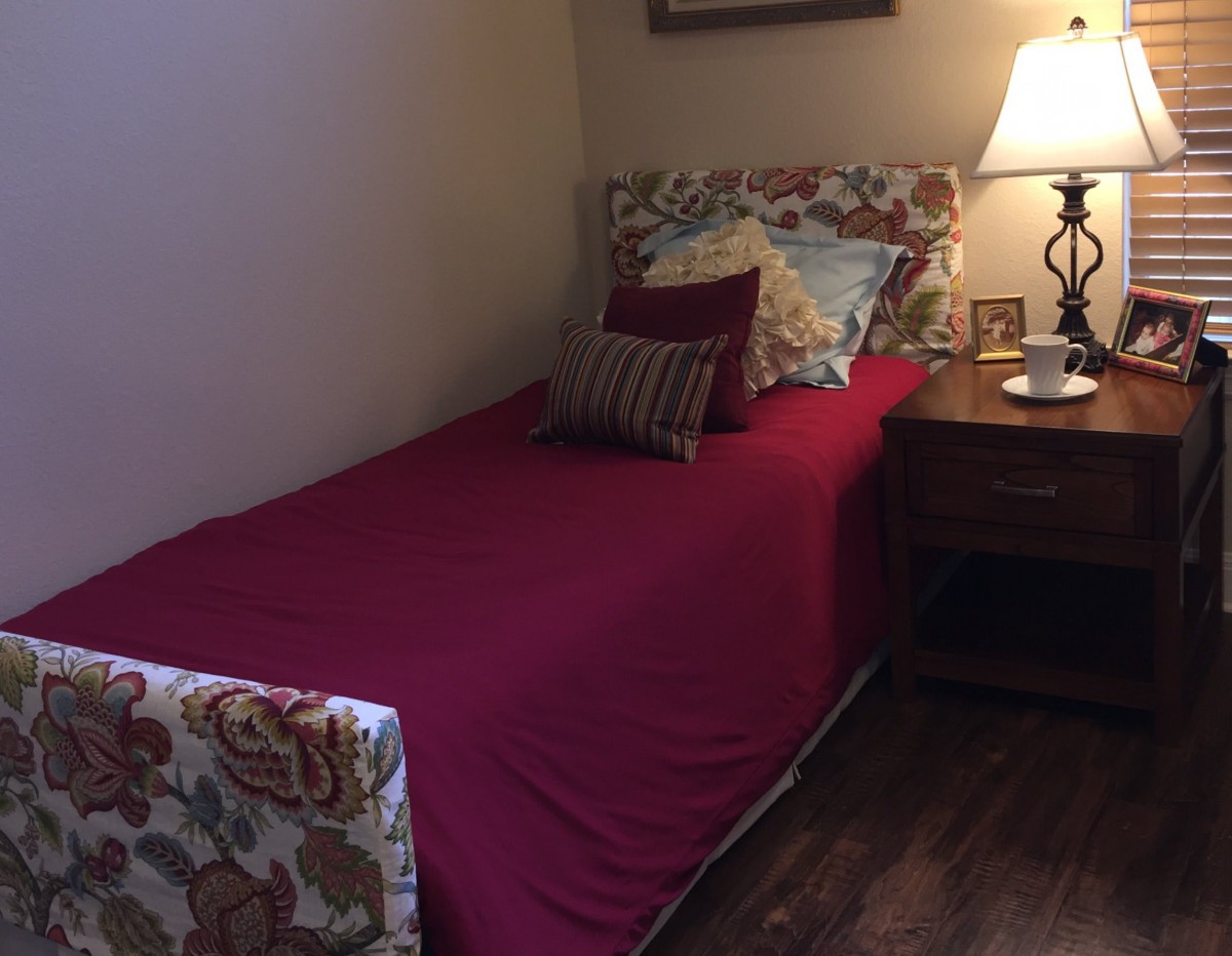 A cozy bedroom with a single bed and a nightstand featuring a lamp.