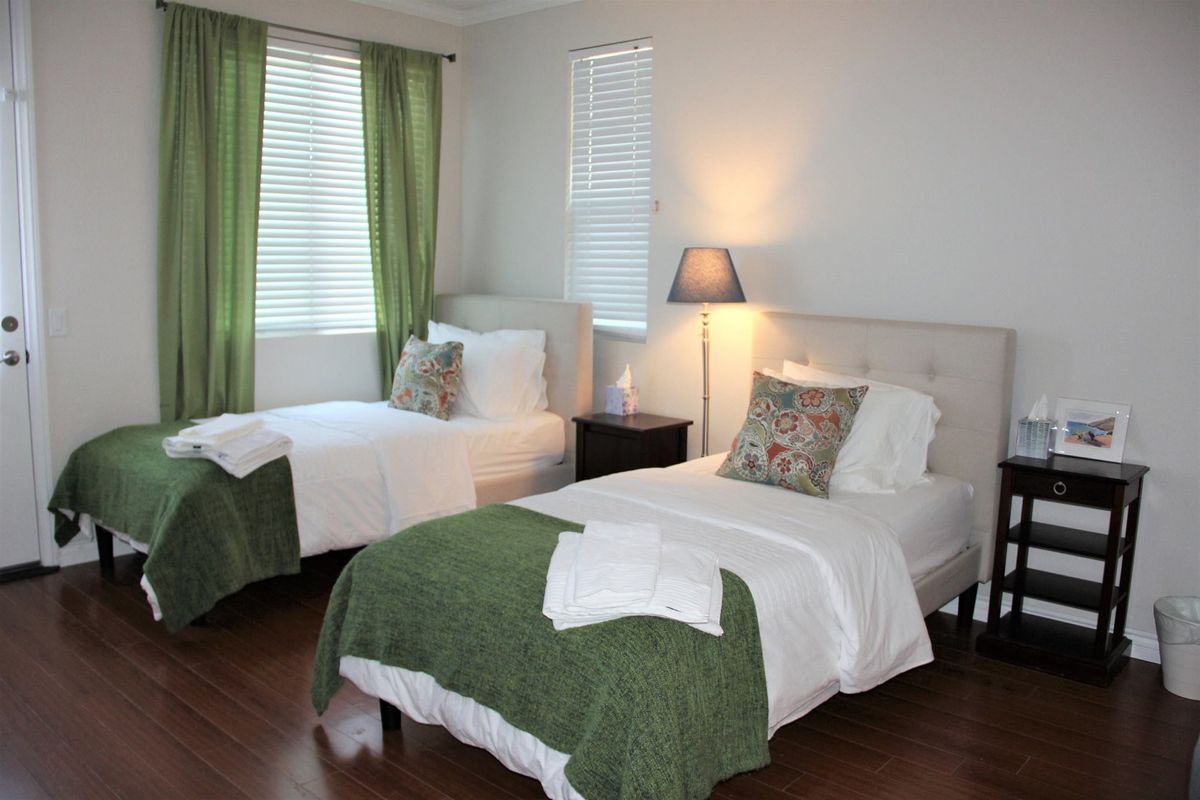 A cozy bedroom with twin beds dressed in green bedding and white sheets, complemented by a nightstand and lamp.
