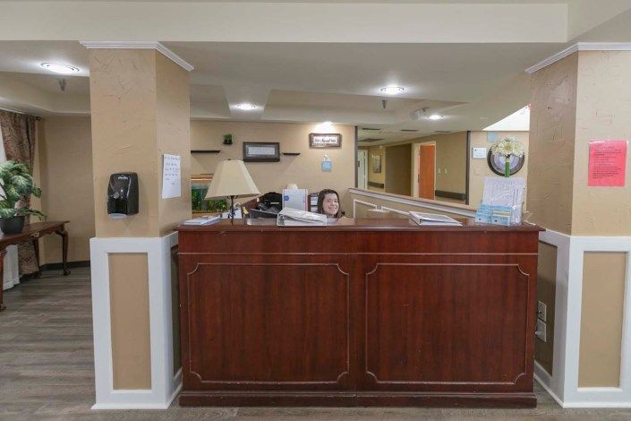A reception area with a wooden desk and a person seated behind it in a lobby setting.