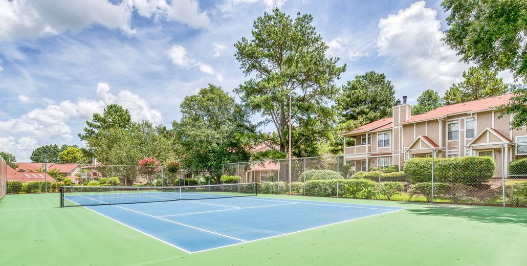 A sunny day at a residential tennis court surrounded by trees and houses.