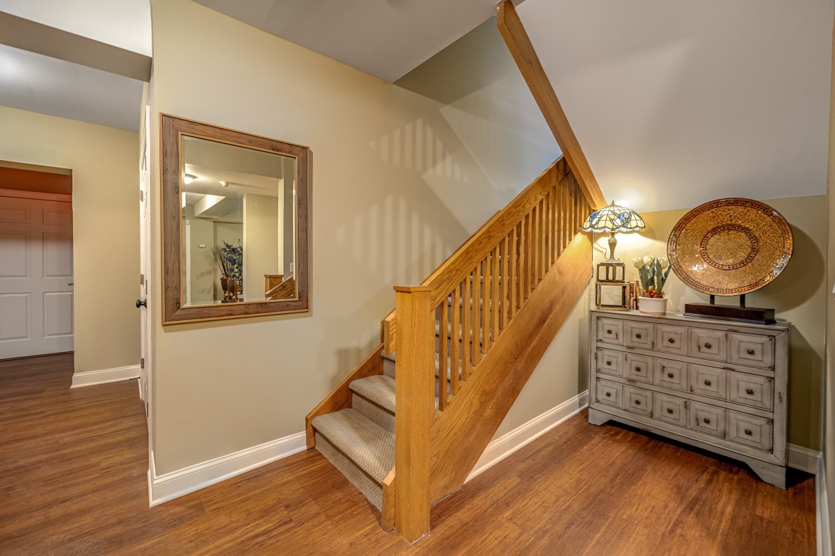 A cozy home interior featuring a wooden staircase with carpeted steps, a large mirror on the wall, and a decorative lamp on a chest of drawers.
