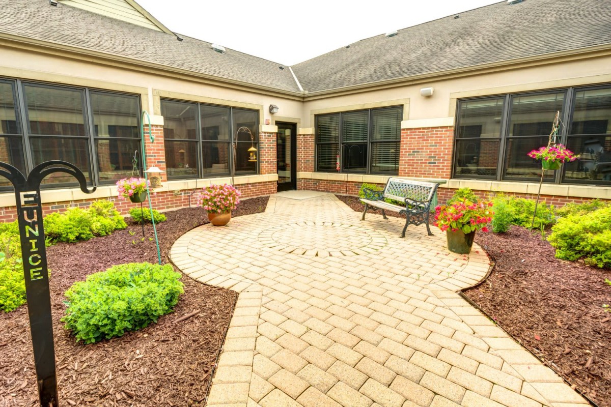 A serene courtyard with a paved path, neatly landscaped plants, and a bench for relaxation.