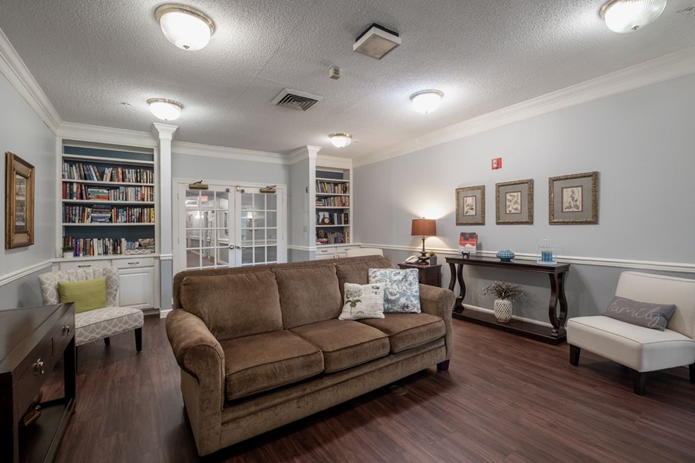 A cozy living room with a brown sofa, hardwood floors, and well-stocked bookshelves.
