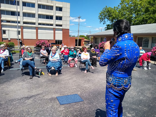 A performer in a blue sequined costume engages with an audience during an outdoor music event.