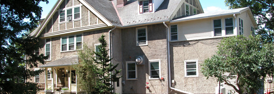 A residential house with multiple windows and a sloped roof, partially obscured by a tree.