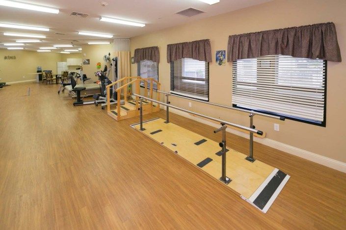 A physical therapy room equipped with parallel bars and gym equipment for rehabilitation exercises.