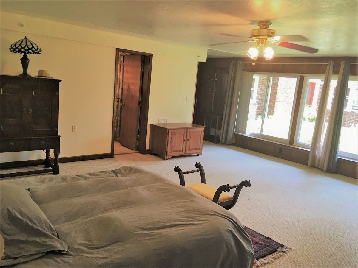 A spacious bedroom with a bed, large windows, and ceiling fan.