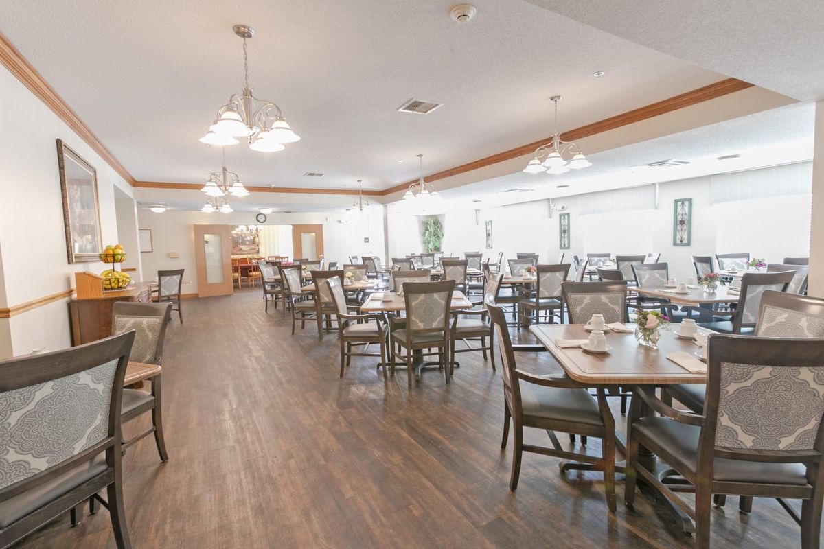 A spacious dining room with multiple tables and chairs, featuring wooden flooring and bright lighting.