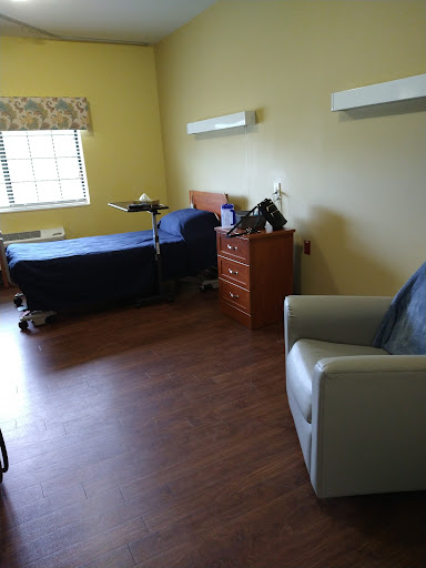 An interior view of a hospital or rehabilitation room featuring a bed, chair, and storage.