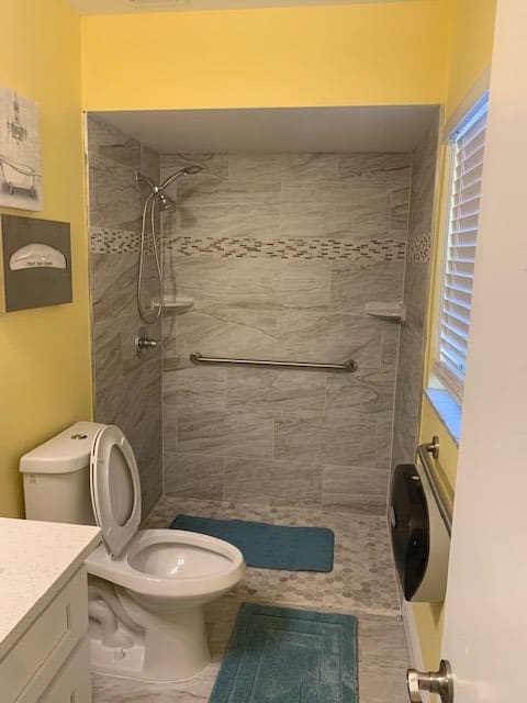 A compact bathroom featuring a tiled shower area with a grab bar, a toilet, and yellow-painted walls.