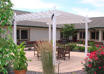 A wooden pergola covering an outdoor seating area with chairs, surrounded by a garden and plants.