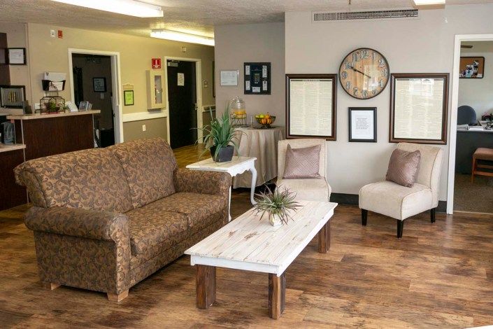 A cozy living room with a sofa, chairs, and a coffee table, decorated with wall art and a clock.