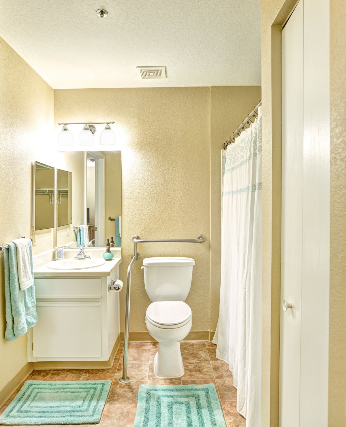 A clean, well-lit bathroom with a toilet, sink, mirror, and shower area.