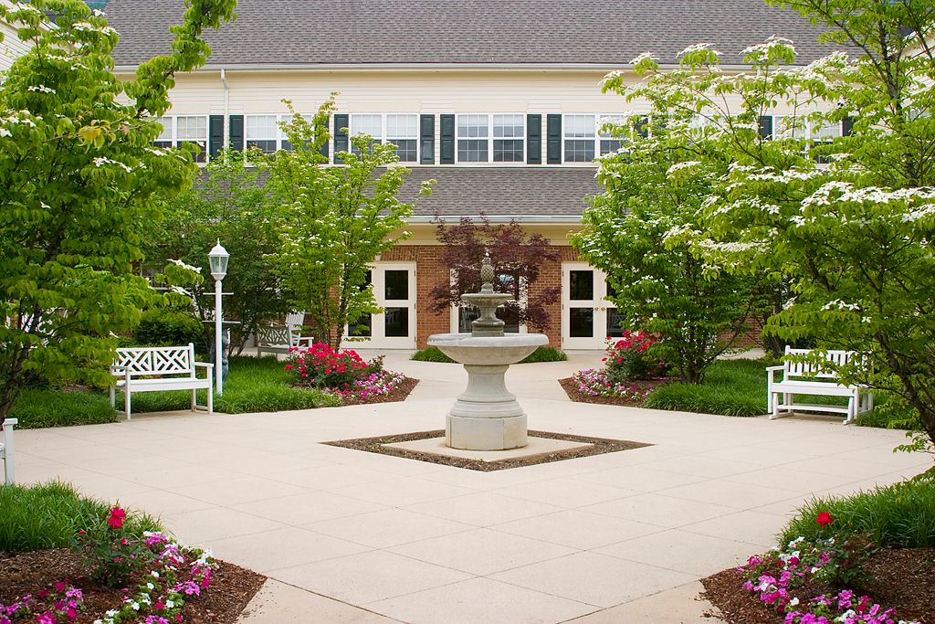 A peaceful courtyard with a central fountain surrounded by a well-maintained garden and building.