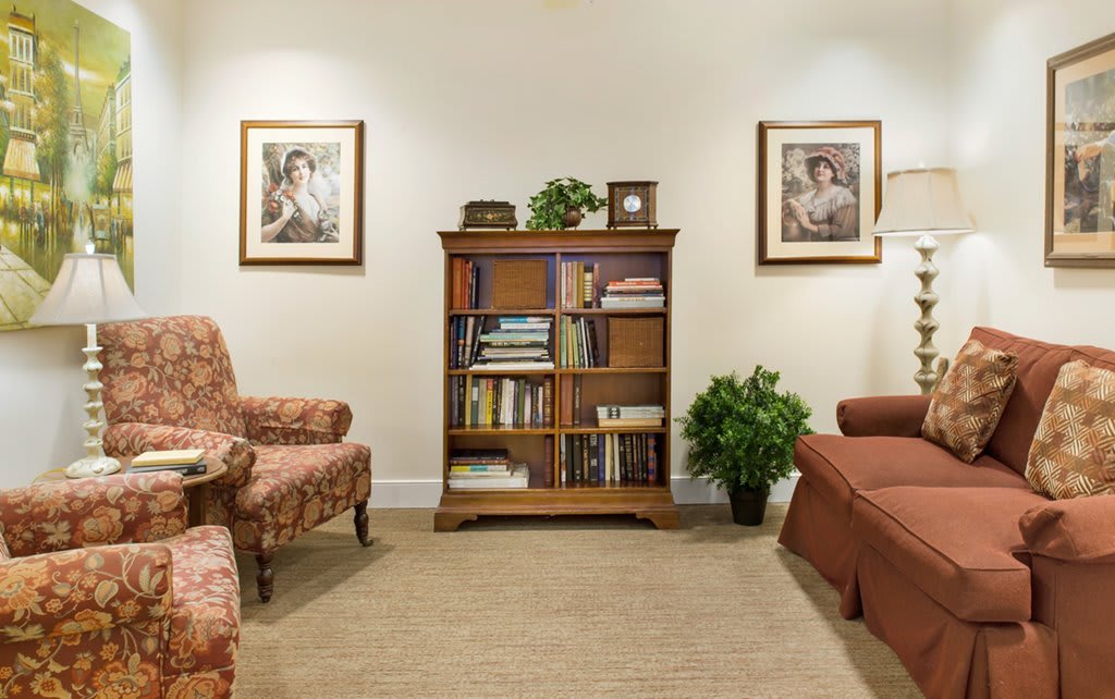 A cozy living room with a wooden bookshelf, armchairs, and framed artwork on the walls.