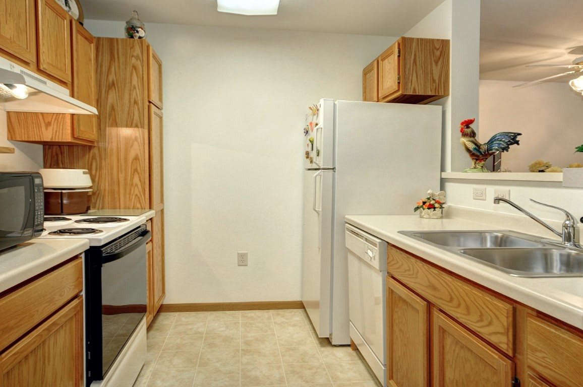 A compact kitchen with wooden cabinets, white appliances, and a clean countertop.