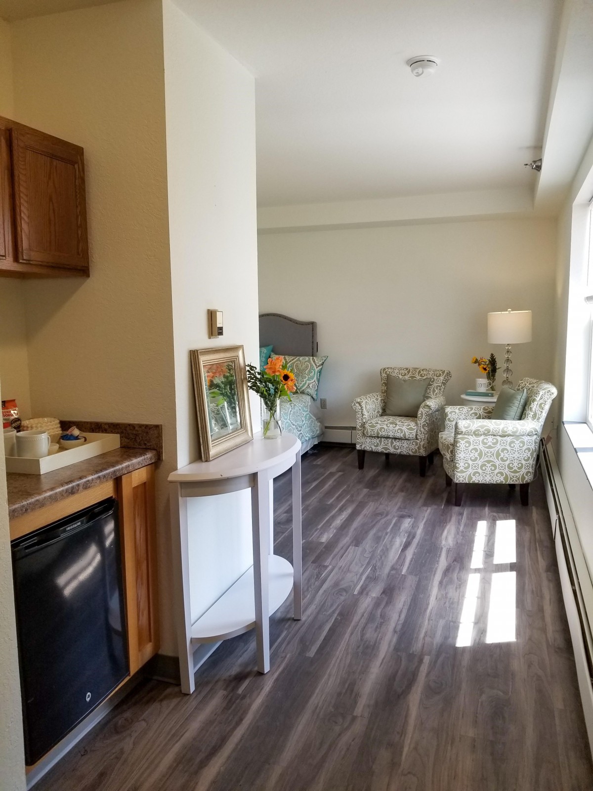 A cozy room with a kitchenette, seating area, and large window allowing natural light.