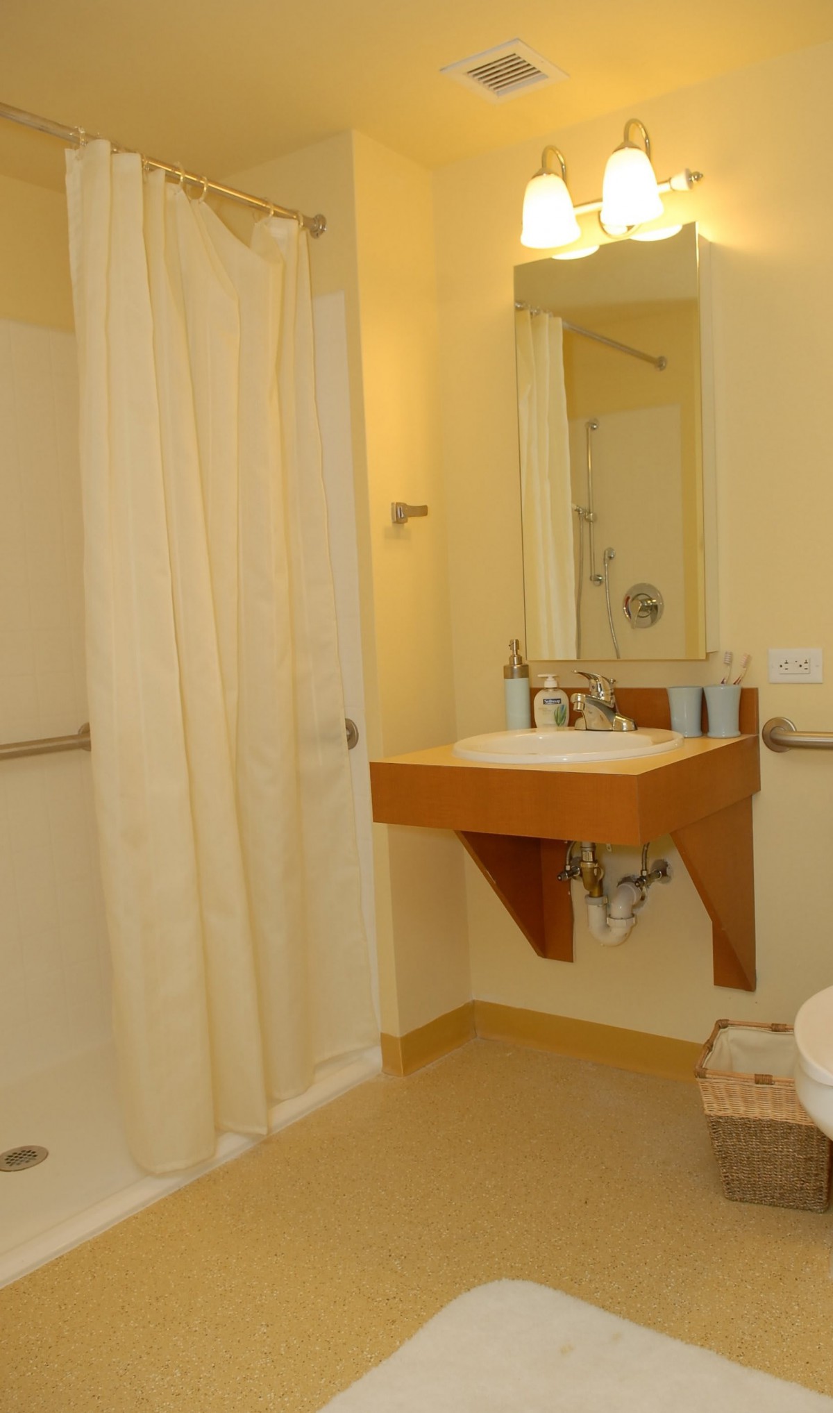 A hotel bathroom featuring a wall-mounted sink, mirror, and shower area with a curtain.