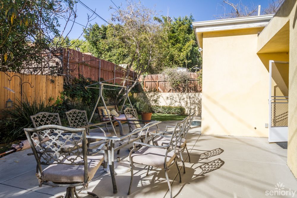 A sunny patio with metal chairs and a view of a garden.