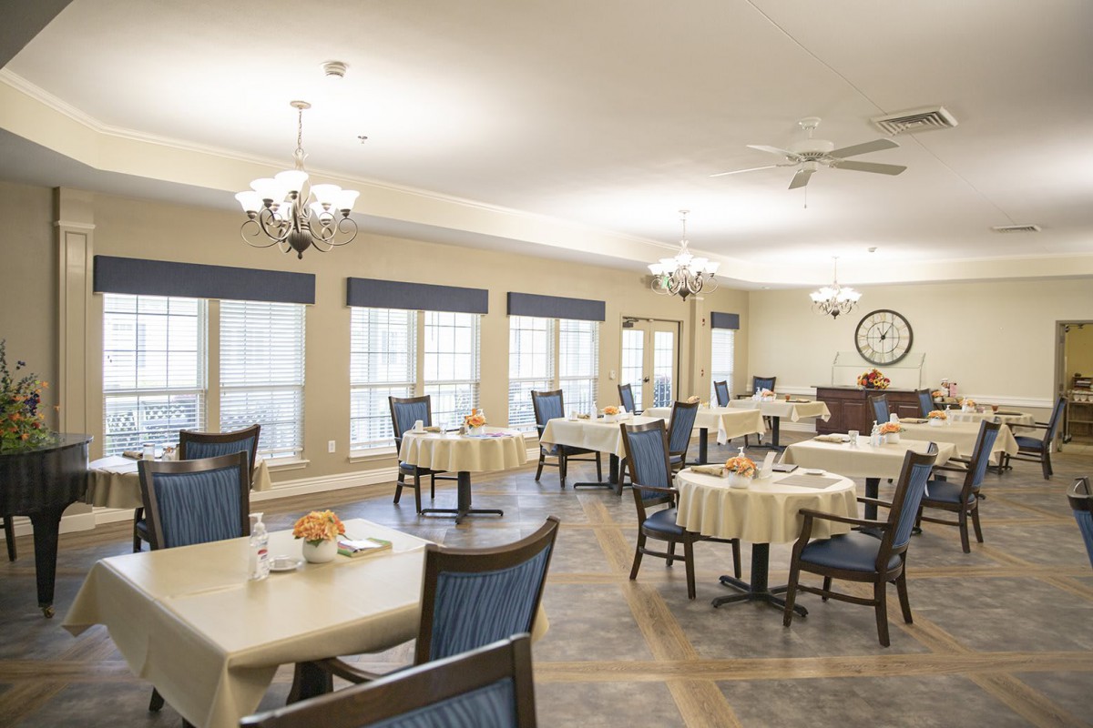 A spacious dining area with neatly arranged tables and chairs, featuring elegant lighting and large windows.