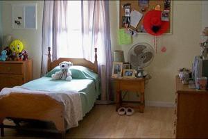 A cozy bedroom with a single bed and stuffed teddy bear by the window, featuring a nightstand with personal items and decorations.