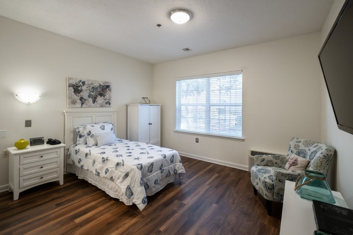 A minimalist bedroom with a single bed, white furniture, and hardwood flooring.