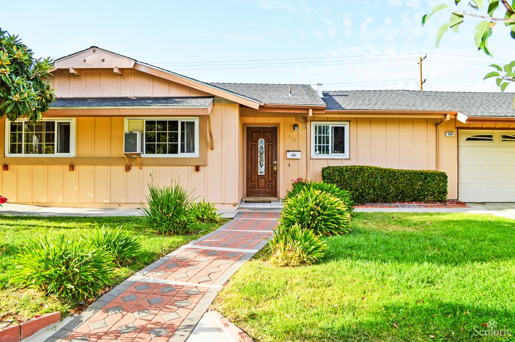 A charming suburban single-story house with a well-maintained lawn and brick pathway.
