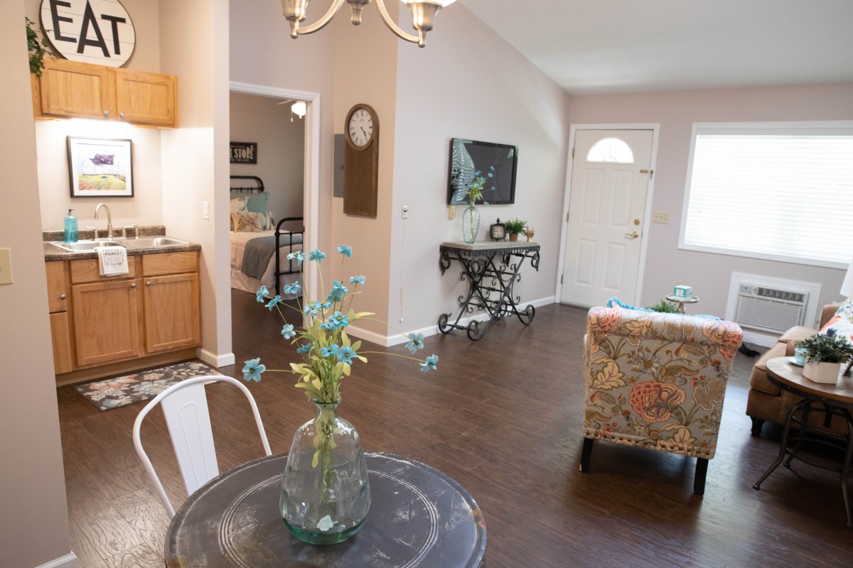 A cozy living room with a dining table, floral armchair, and a welcoming entryway.