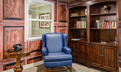 A cozy home office corner featuring a blue armchair and wooden bookshelves.