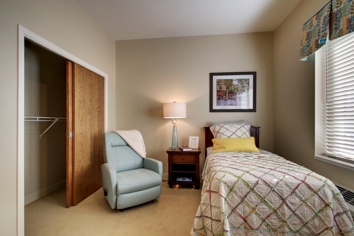 A cozy bedroom with a single bed, armchair, and nightstand.
