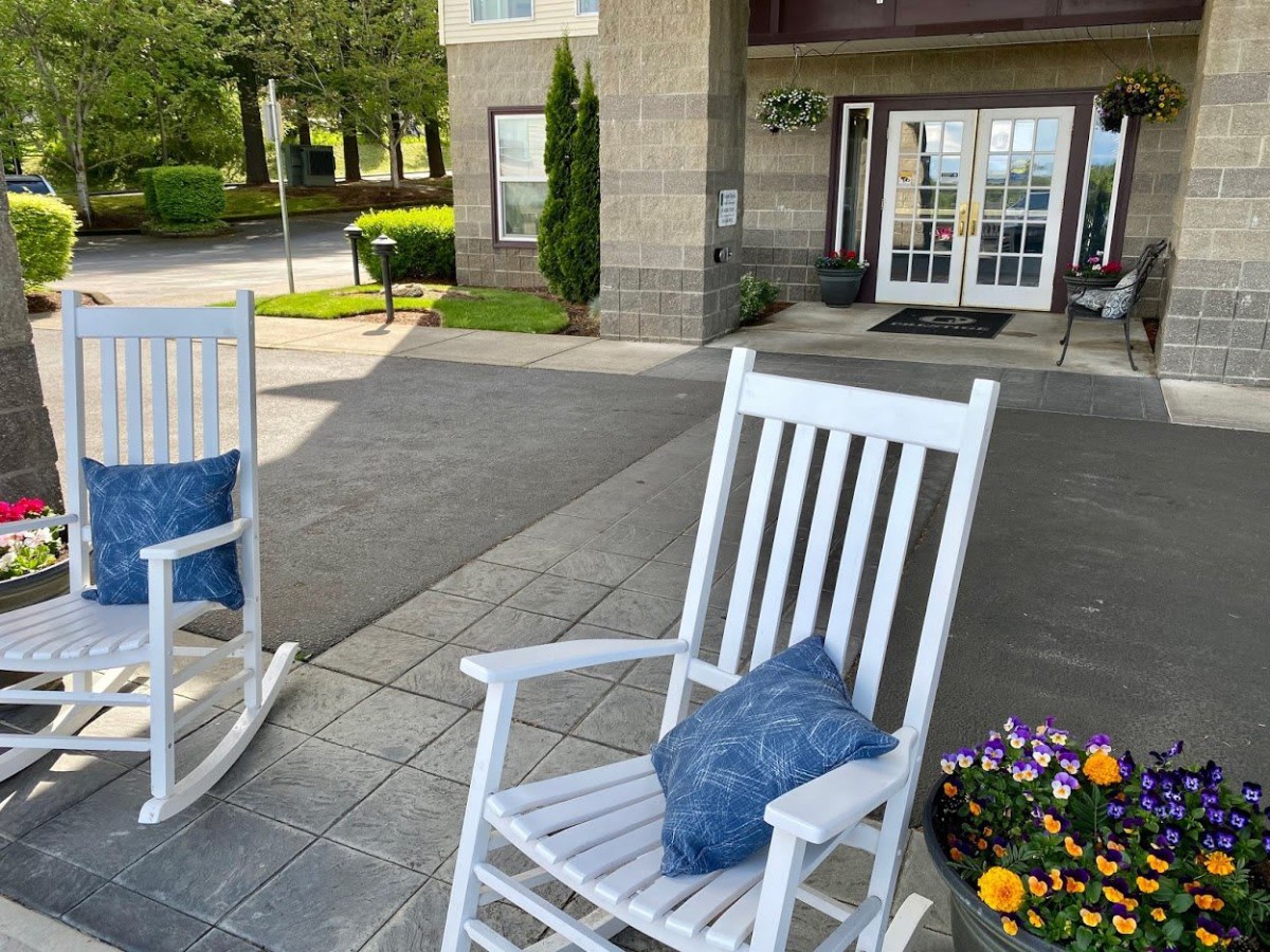 A cozy porch entrance with white rocking chairs and colorful flowers.