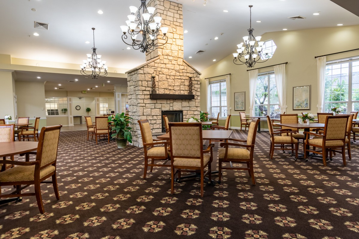 A cozy dining area with a central stone fireplace, chandeliers, and elegant furniture.
