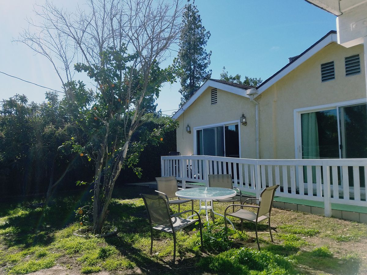 A cozy house with a garden patio featuring outdoor furniture and surrounding greenery on a sunny day.