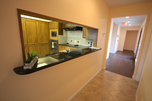 A modern open-concept kitchen featuring wood cabinets and a granite countertop, viewed from the hallway.