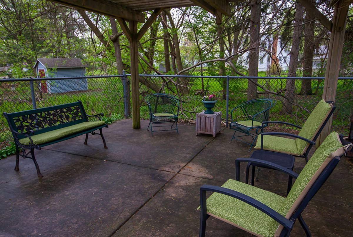 A cozy outdoor seating area under a wooden gazebo surrounded by lush greenery.