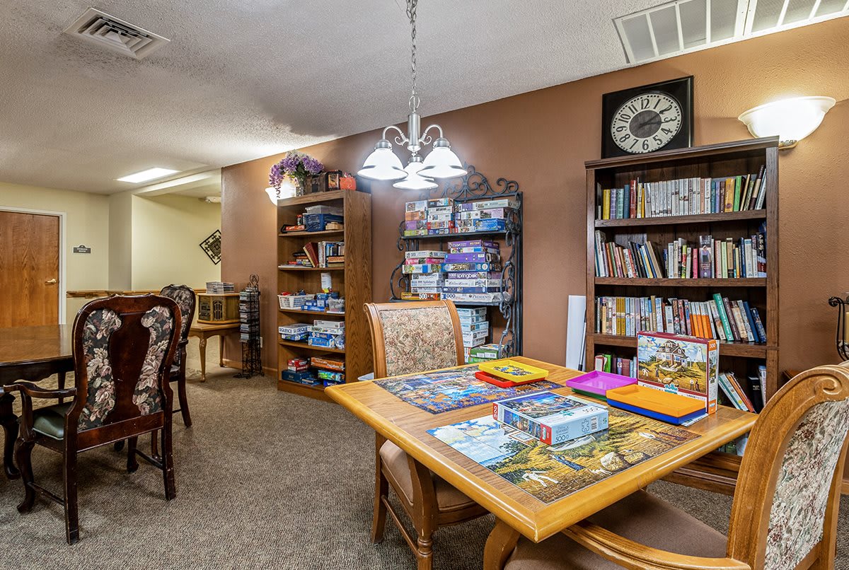A cozy library interior with bookshelves and a reading table surrounded by chairs.