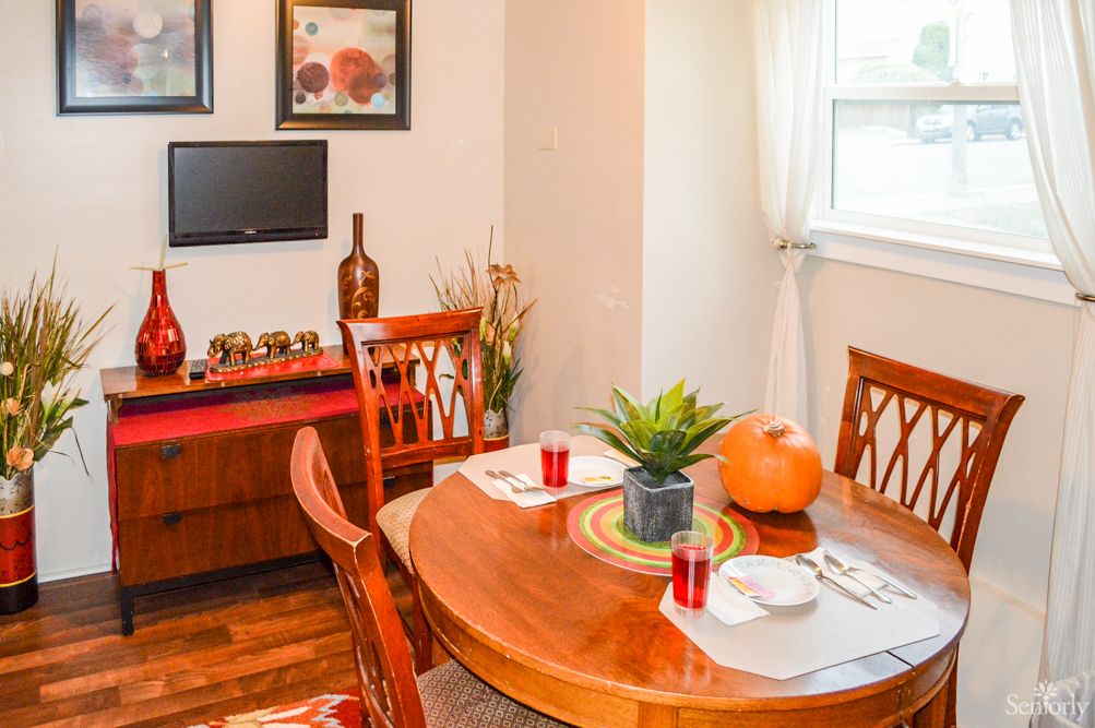 A cozy dining room setup featuring a wooden table with chairs, adorned with a pumpkin and potted plant as centerpiece decor.