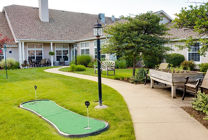 A peaceful garden setting featuring a mini golf course, benches, and a pathway leading to a building.