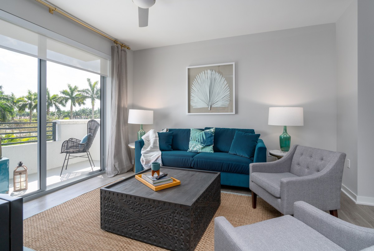 A modern living room with a blue sofa, gray armchair, and large windows providing natural light.