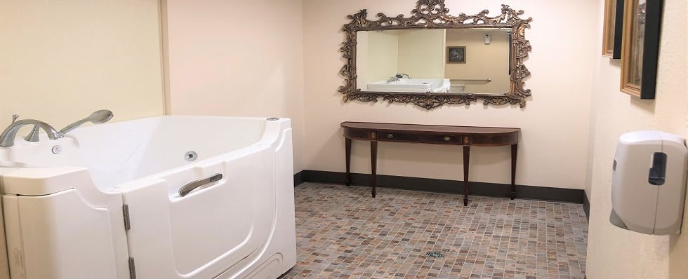 A spacious bathroom with a walk-in bathtub, ornate mirror, and tiled flooring.
