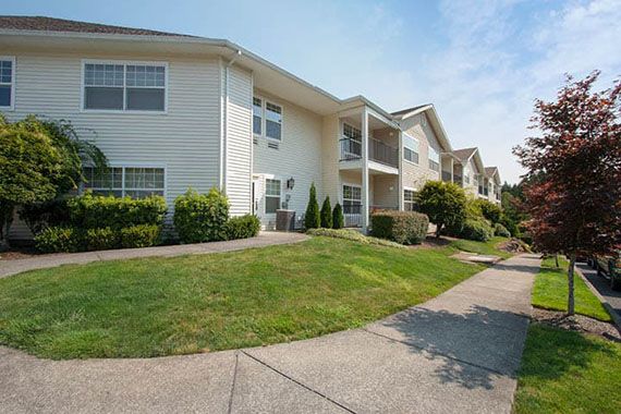A suburban apartment building with well-maintained landscaping and a sidewalk.
