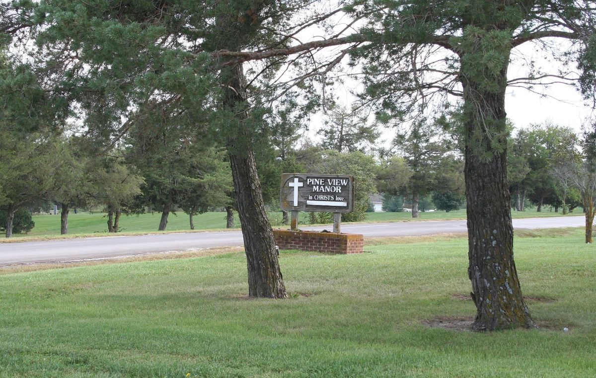 A church sign surrounded by trees and grass near a road.