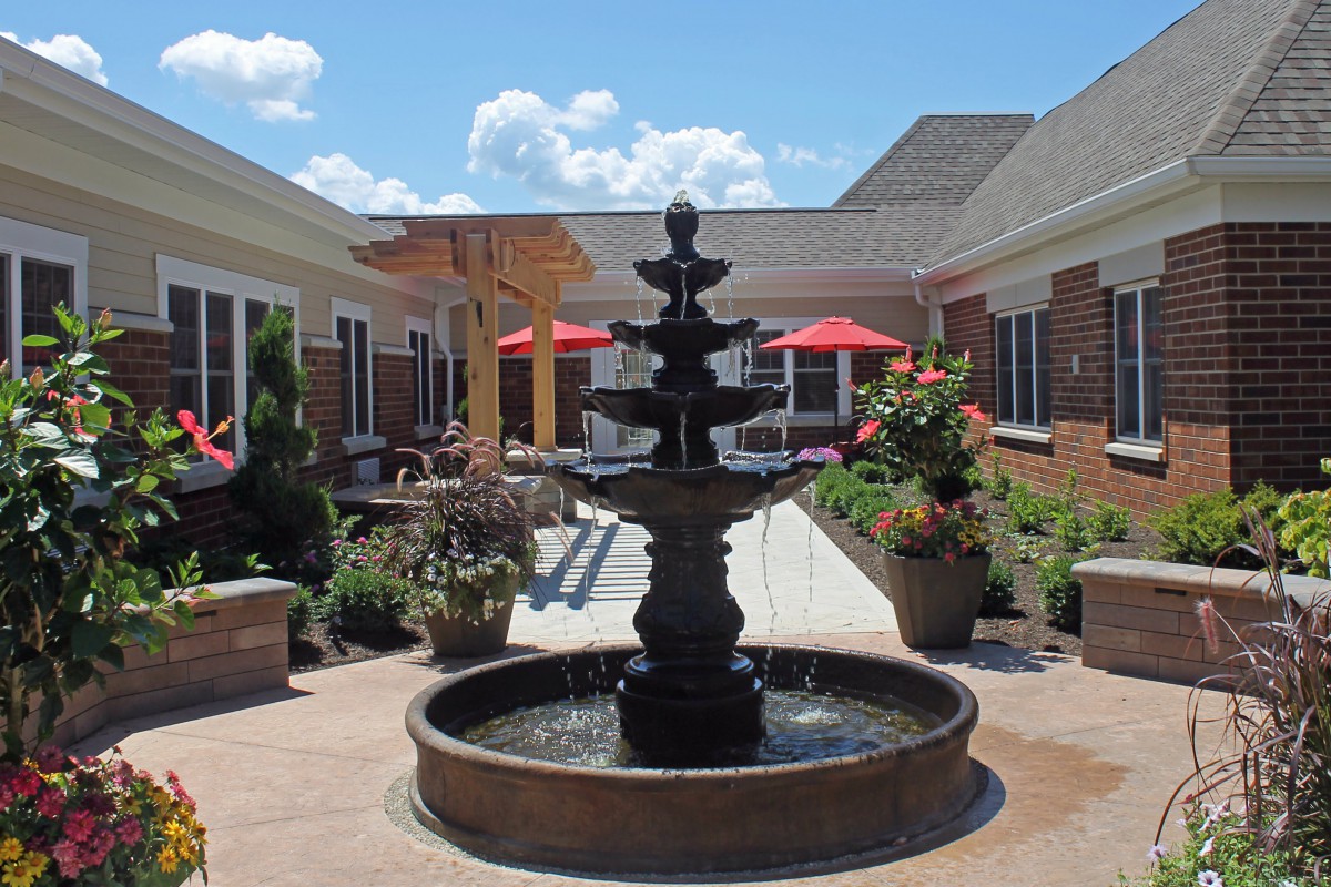 A serene courtyard featuring a multi-tiered fountain surrounded by greenery and patio seating.