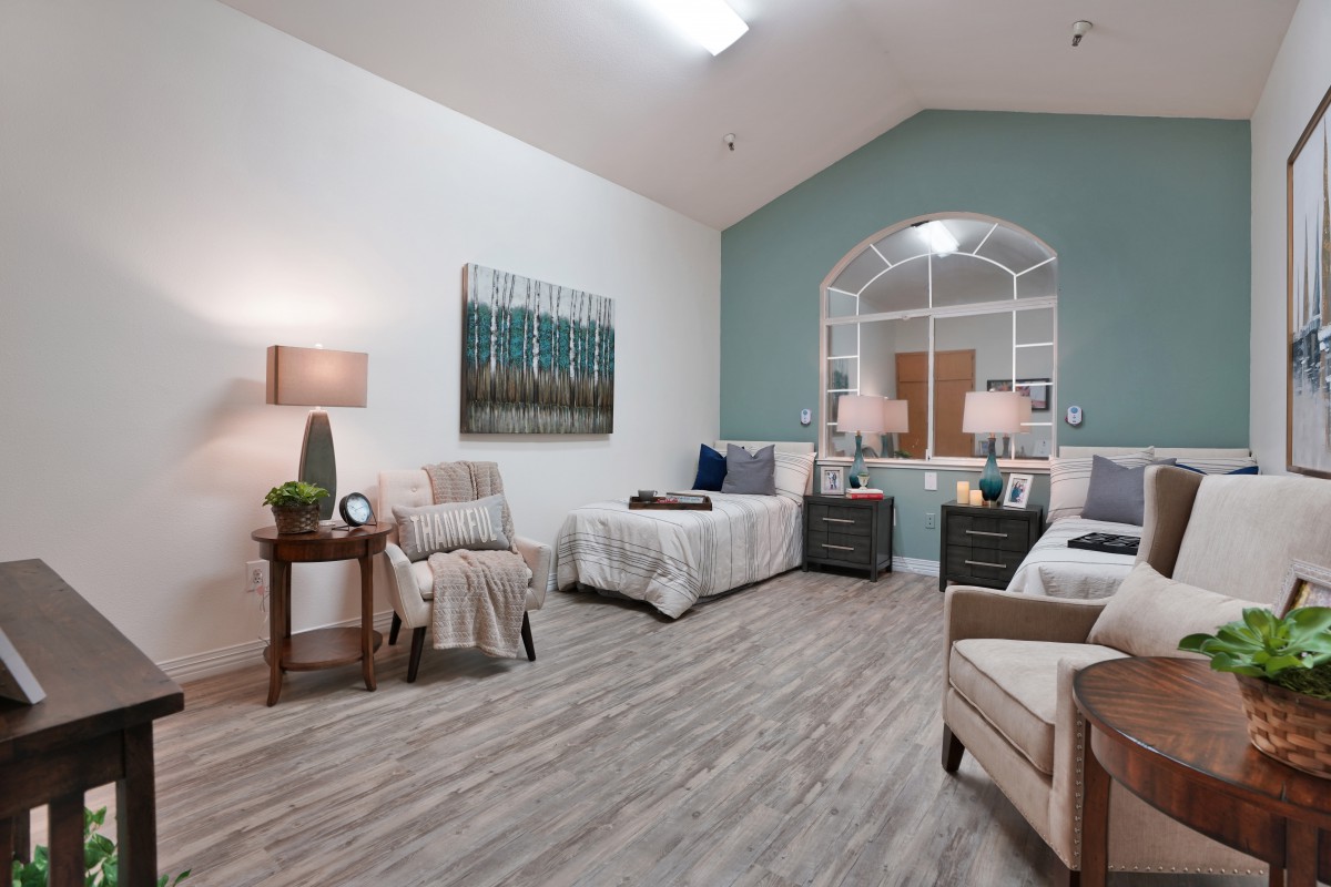 A well-furnished bedroom featuring two beds, comfortable chairs, modern lamps, artwork on the walls, and a stylish wooden floor.