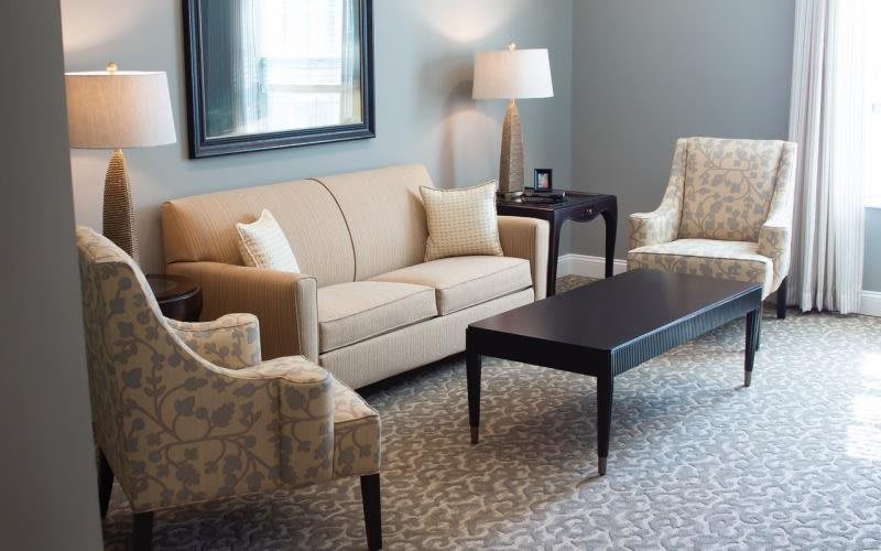 A well-appointed living room featuring a beige sofa, patterned armchairs, a dark coffee table, and a standing lamp.